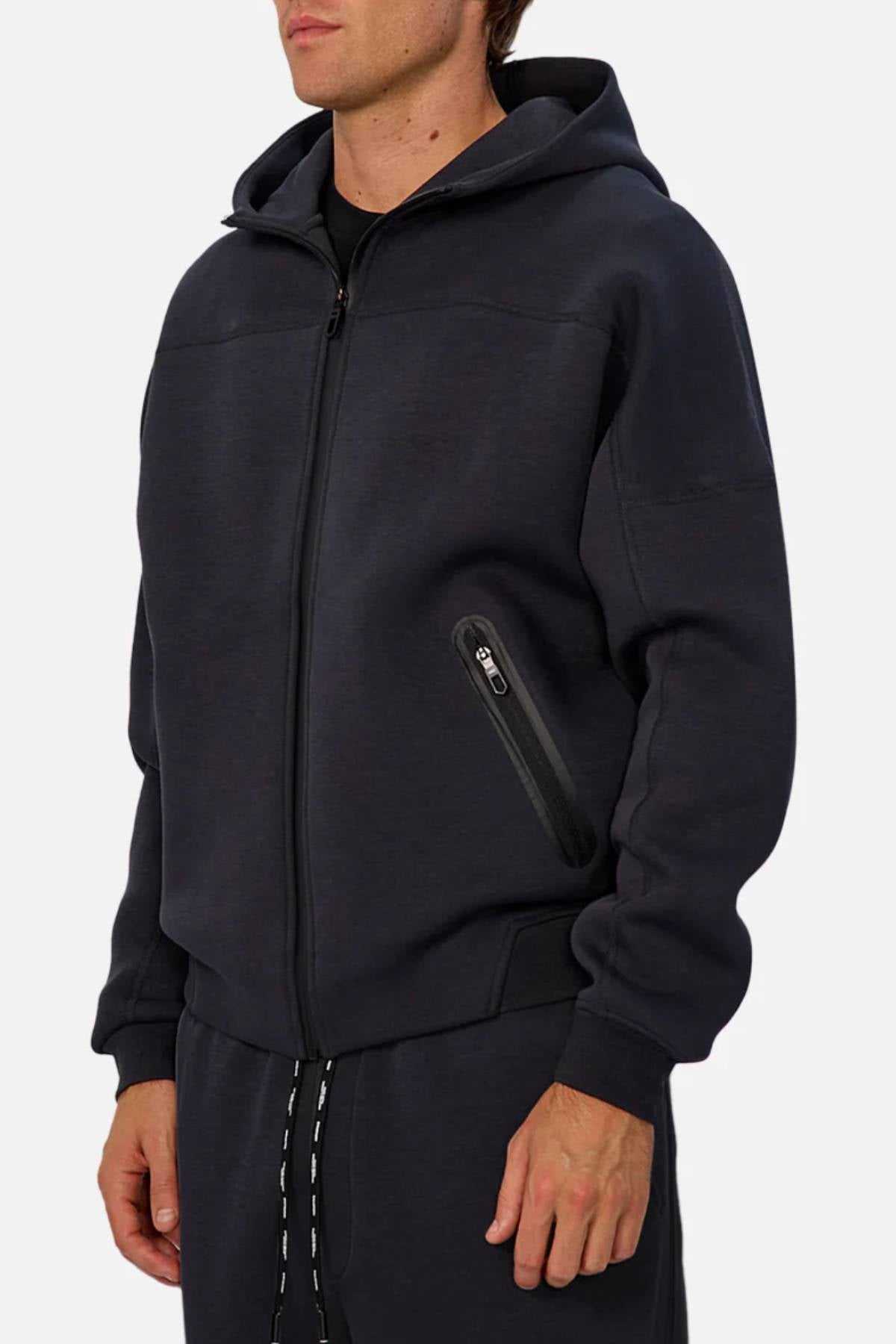 A person wearing Industrie The Washington Zip Thru with a hood and zippered pockets, paired with matching black joggers—ideal for daily wear—stands against a plain light background.