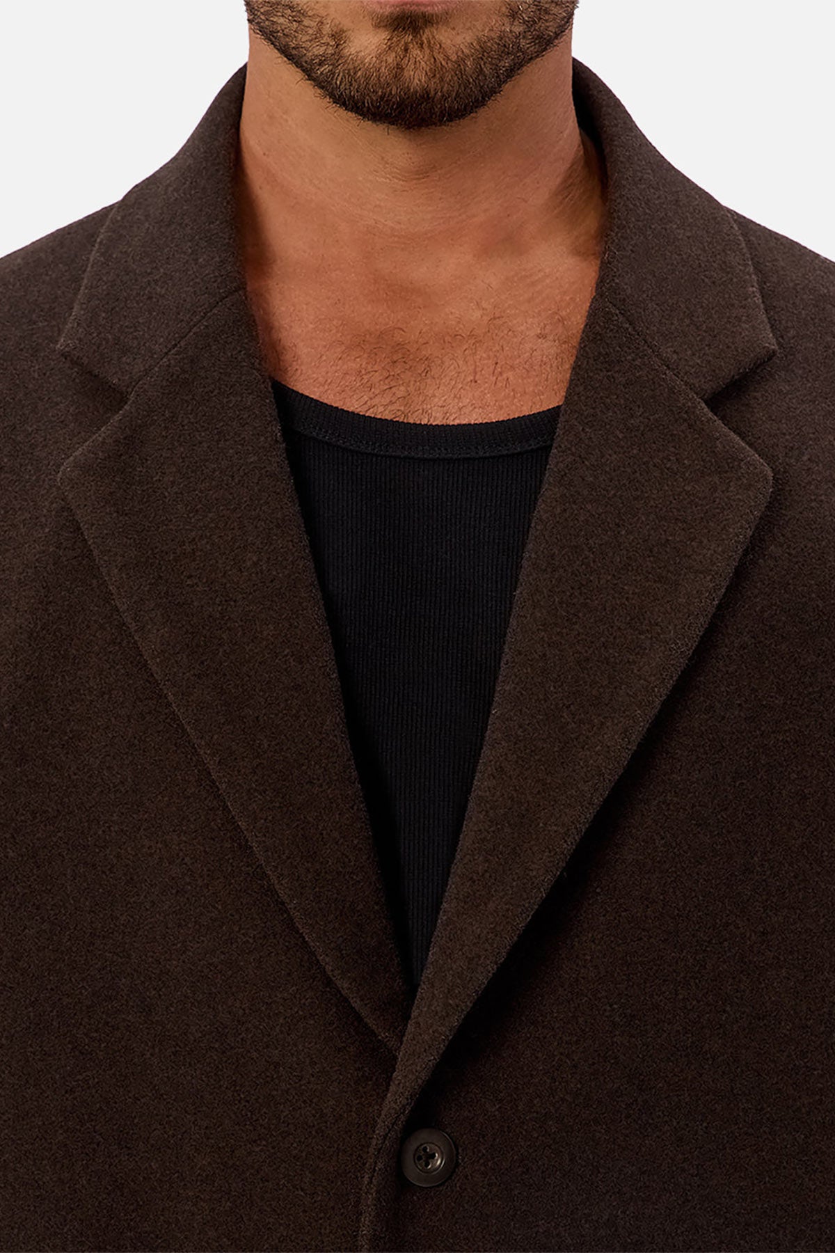 A man wears the Industrie The Wool Blend Jacques Coat in dark brown over a black ribbed shirt. The close-up highlights the coat’s lapel, collar, and a button, with his face partially visible.
