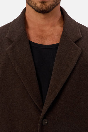 A man wears the Industrie The Wool Blend Jacques Coat in dark brown over a black ribbed shirt. The close-up highlights the coat’s lapel, collar, and a button, with his face partially visible.