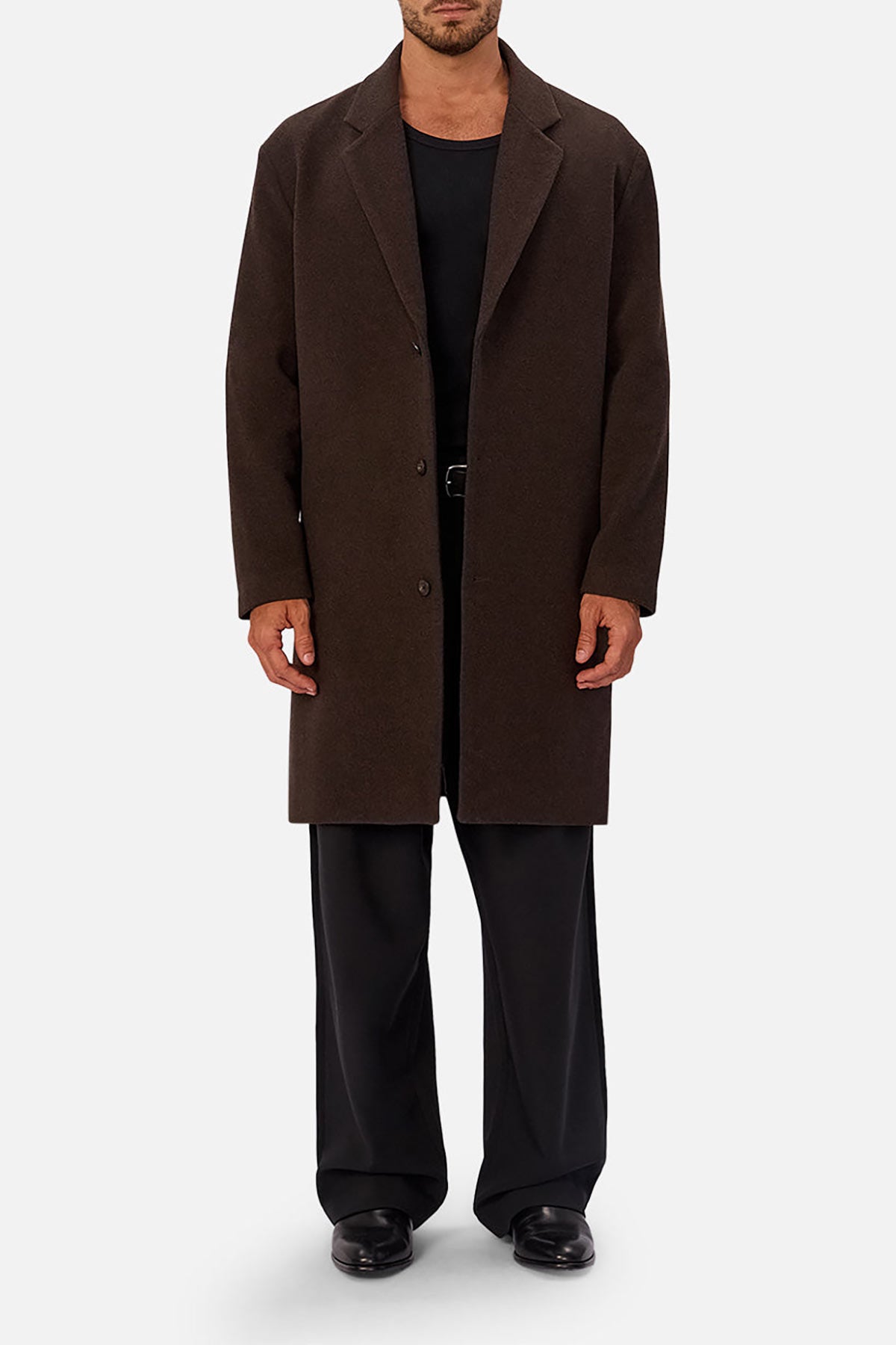 A man wears the Industrie The Wool Blend Jacques Coat in dark brown over a black shirt, black wide-leg pants, and black shoes. He stands against a plain light background with his face turned away from the camera.