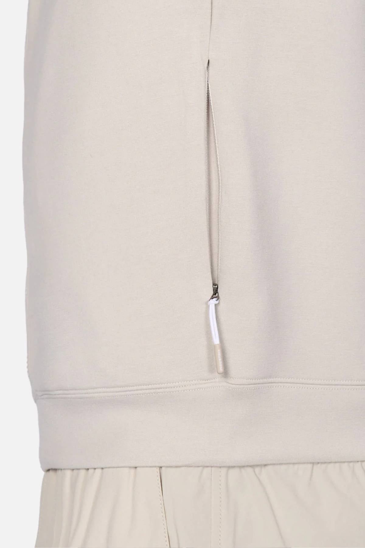 Close-up of the Industrie The Zip Thru Track Top in light beige, showing a vertical zippered side pocket. The hem overlaps matching beige pants with an elastic waistband for a sleek, athletic look.