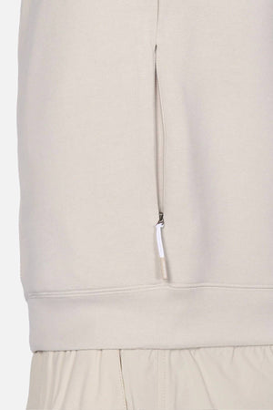 Close-up of the Industrie The Zip Thru Track Top in light beige, showing a vertical zippered side pocket. The hem overlaps matching beige pants with an elastic waistband for a sleek, athletic look.