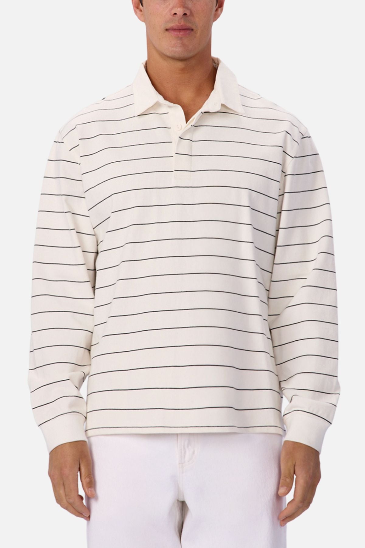 A person wears the Industrie The Ole Miss Rugby Top—a smart casual, long-sleeve cream polo with black stripes—paired with white pants, standing against a simple light background.
