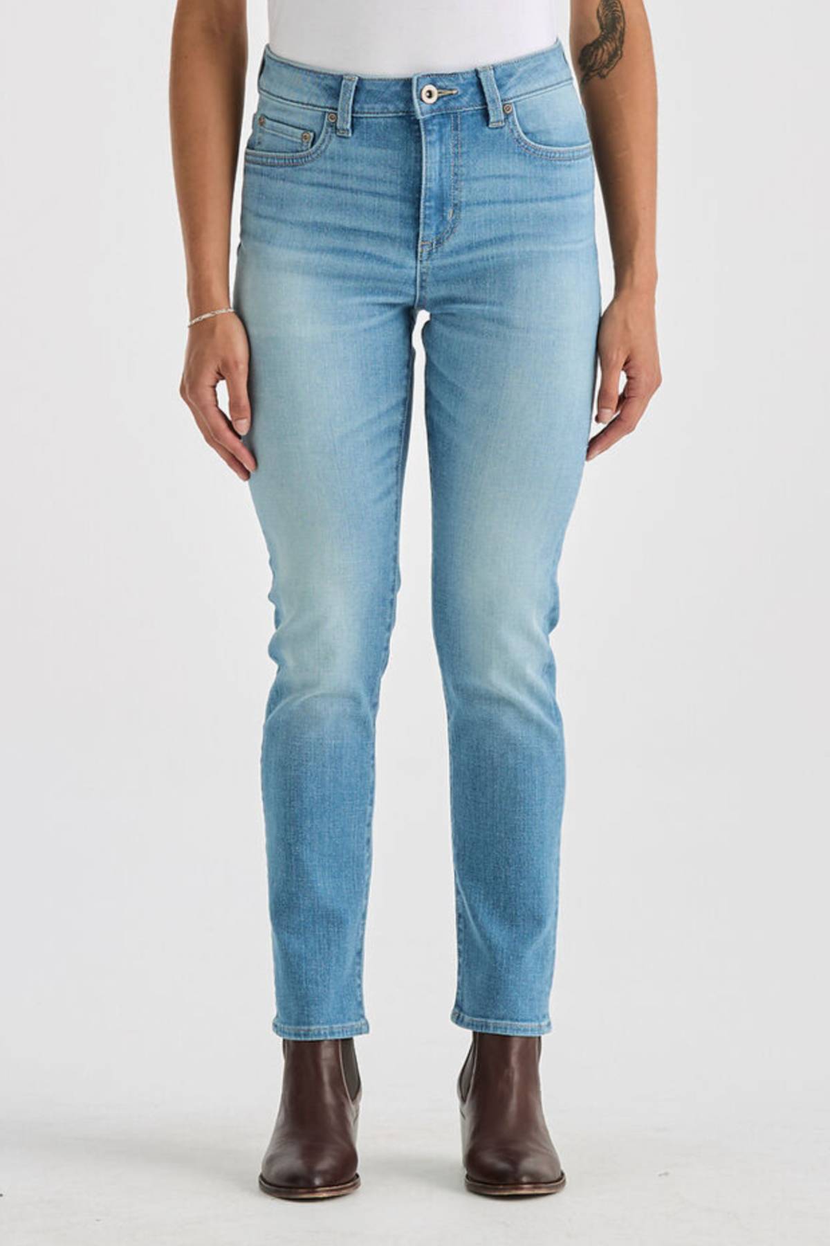 Wearing Lee Originals LMW Mid Rise Slim Jean in light blue, a white top, and brown ankle boots, the model stands against a plain white background with hands by their sides; only the body from shoulders down is visible.