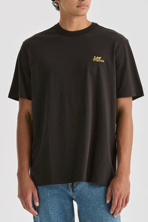Wearing a Lee Originals Relaxed Tee—a black, 100% cotton T-shirt with a relaxed fit and small yellow "Lee Originals" text on the chest—paired with blue jeans, the person stands against a plain light background.