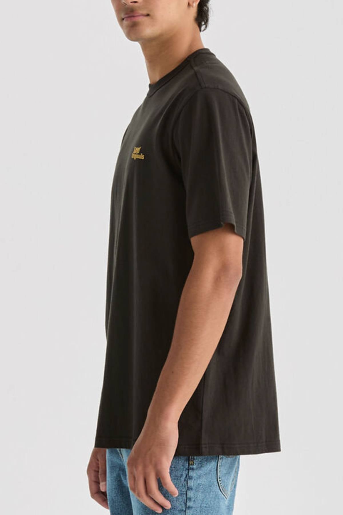 A person stands sideways against a plain light background, showing only their upper half, wearing a black Lee Originals Relaxed Tee and blue jeans.