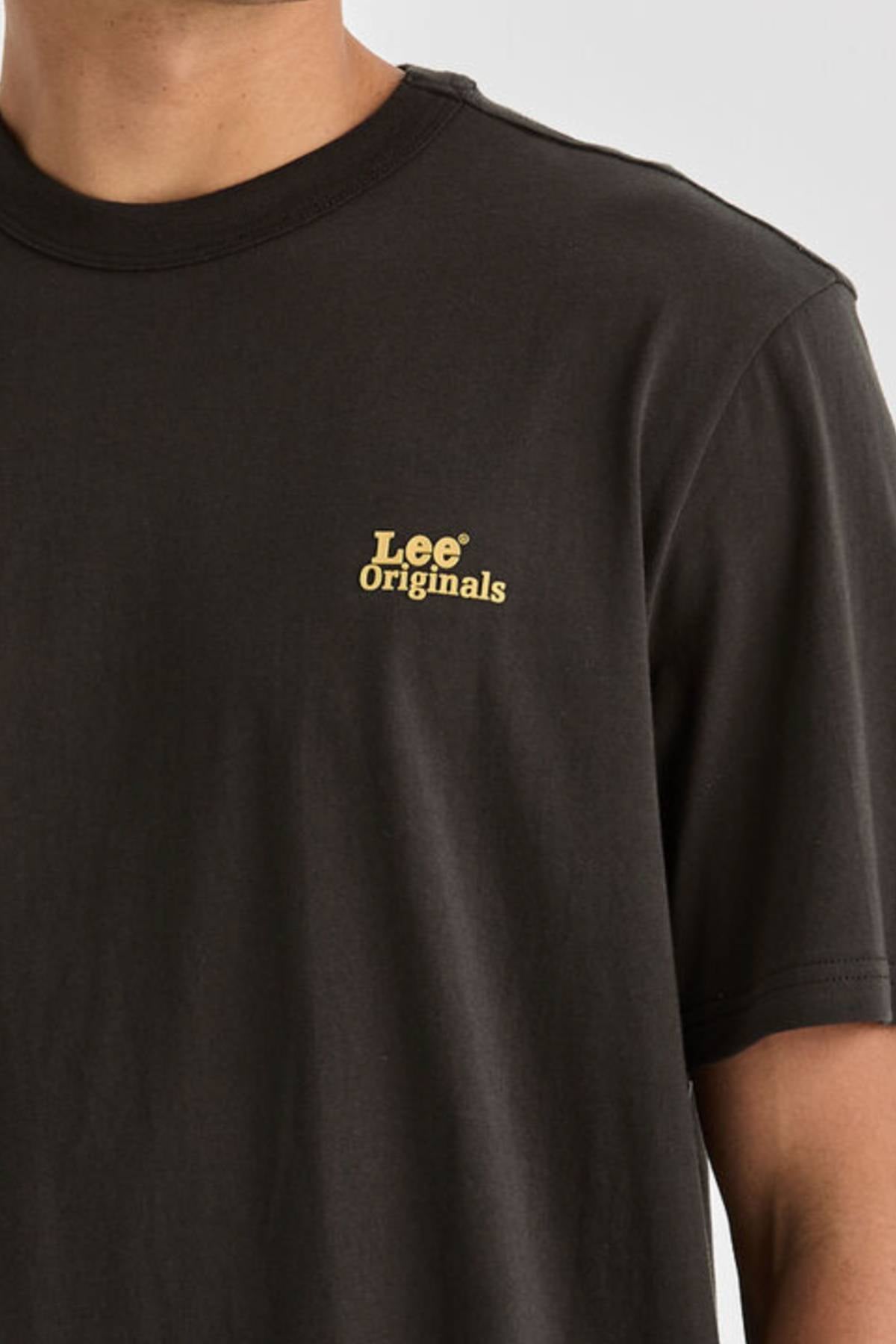 A person is shown from the upper torso up, wearing a relaxed fit Lee Originals Relaxed Tee in plain black with short sleeves and a small yellow "Lee® Originals" logo on the left chest. The T-shirt is made from 100% cotton.