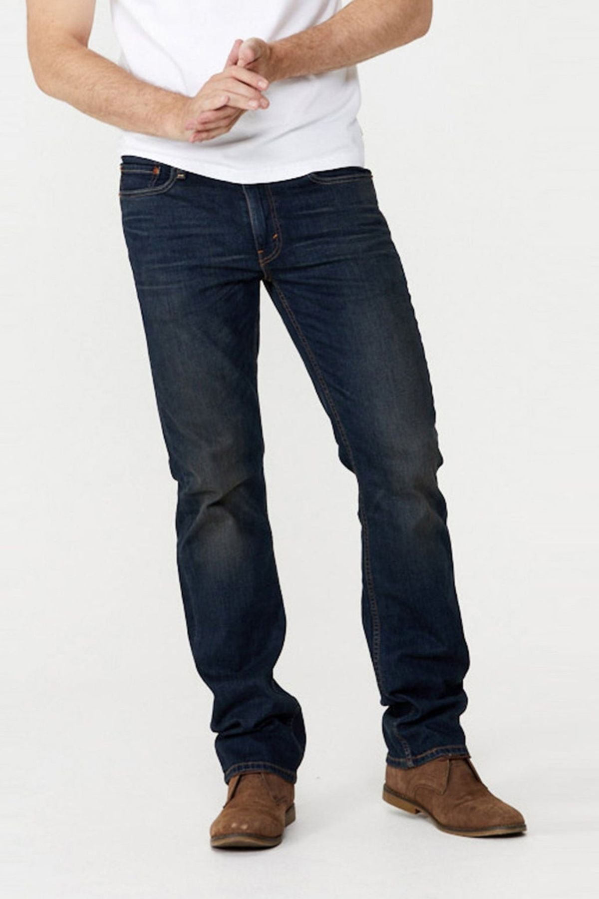 A person wearing a white shirt, Levis 514 Straight Jean in dark blue, and brown suede shoes stands with hands clasped. The photo is cropped at the shoulders, and the background is plain and light-colored.