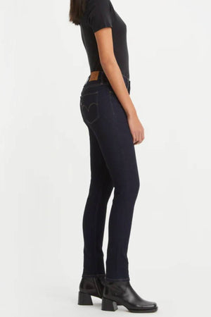 A person stands in profile against a white background wearing a black short-sleeve shirt, Levis 311 Shaping Skinny Jean in dark blue, and black heeled boots.