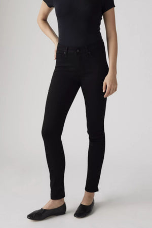 A person stands against a plain background, wearing a fitted black short-sleeve top, Levis 311 Shaping Skinny Jean in black, and black flat shoes. Their face is not visible.
