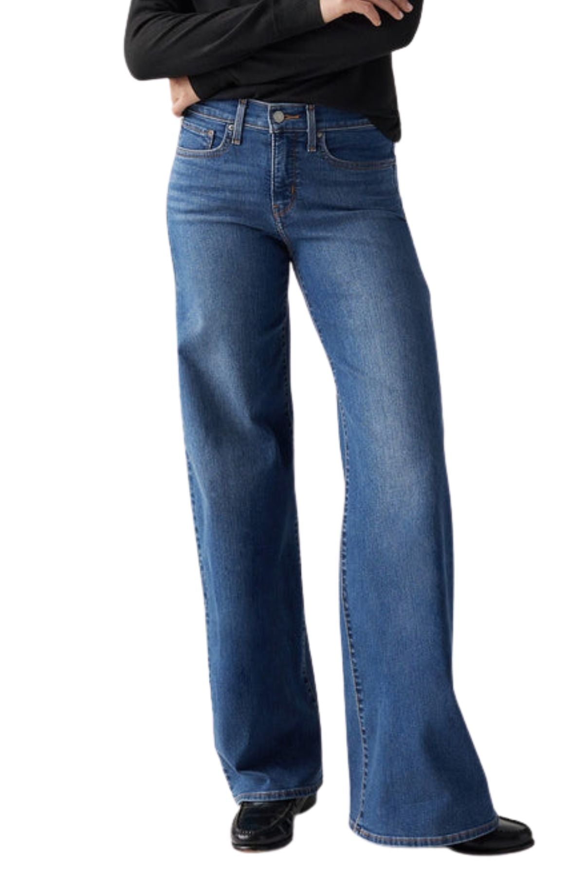 A person in Levis 318 Shaping Wide Leg Jean, black shoes, and a black long-sleeve top poses with arms crossed against a white background.