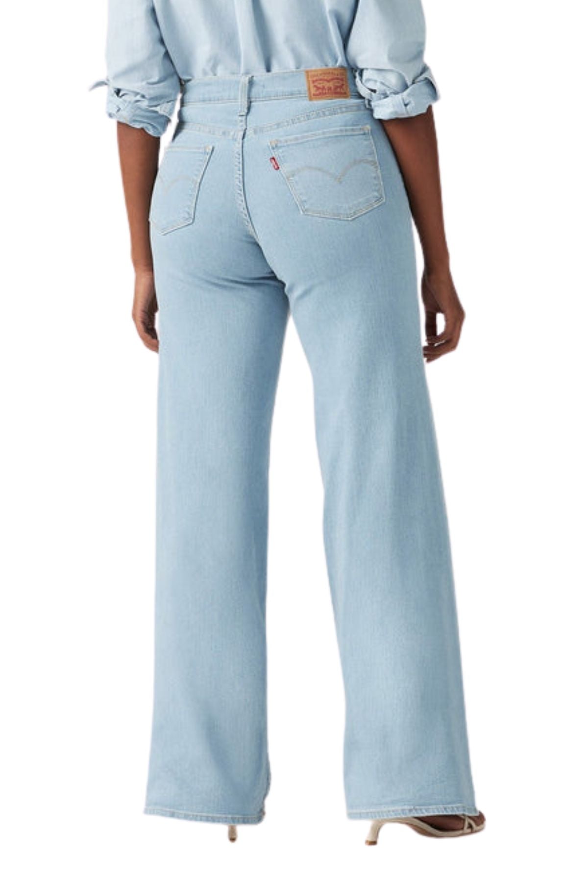 A person wearing Levis 318 Shaping Wide Leg Jean in light blue and a matching rolled-sleeve shirt stands with their back to the camera, highlighting the effortless style of these high-waisted shaping jeans.