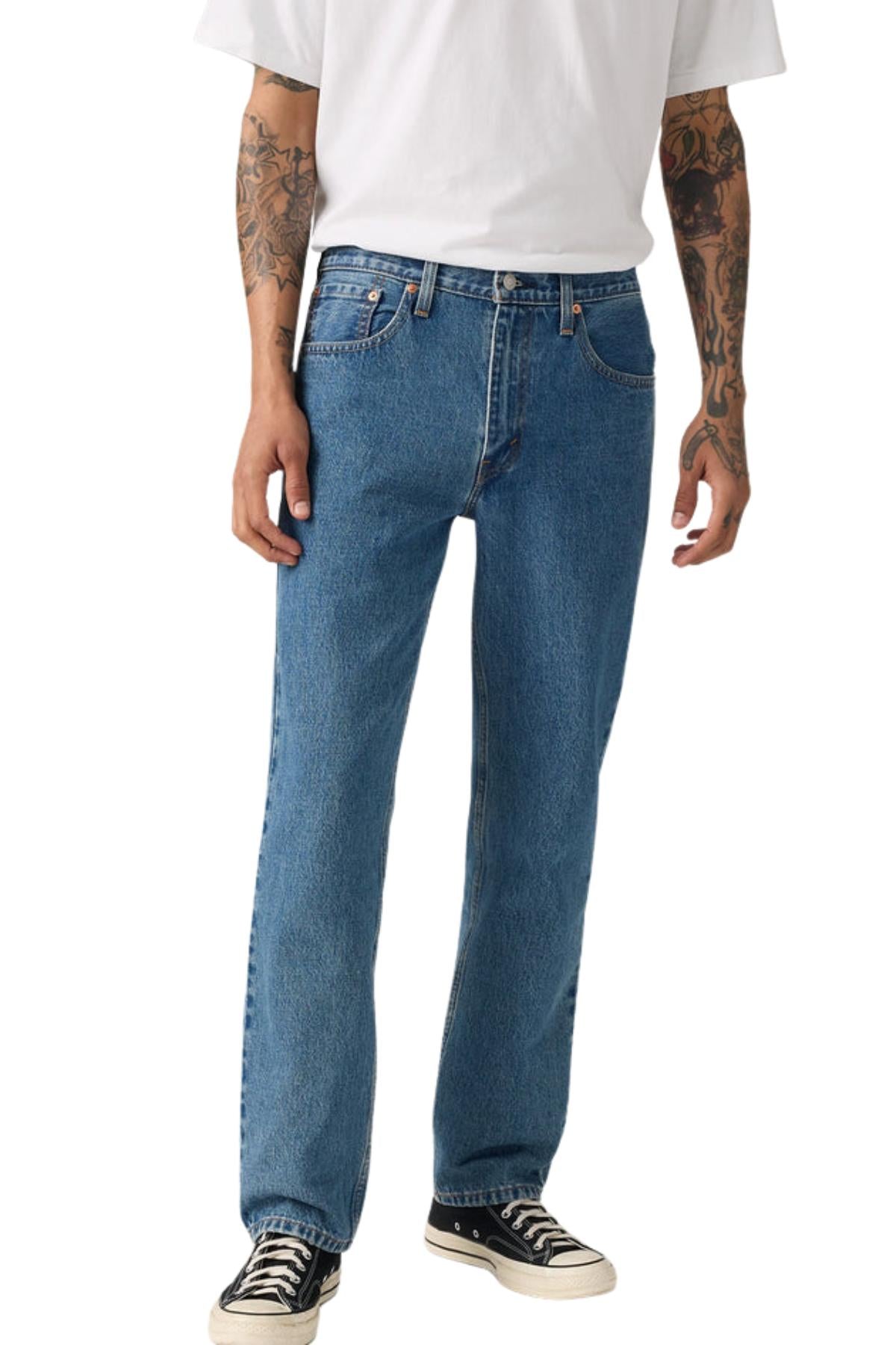 A person wearing a plain white t-shirt, Levis 516 Straight Jeans in stonewash, and black-and-white sneakers. Tattoos are visible on their arms, and only their body from the shoulders down is shown.