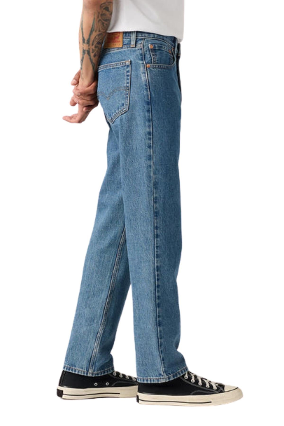 A person wearing Levis 516 Straight Jean and black sneakers stands with hands clasped behind their back. Only the lower body is visible against a plain white background.