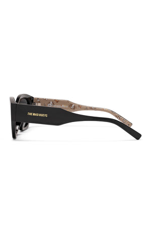 Side view of Liive Cabron Polarised Sunglasses in black with thick arms and smoke lenses. The outer arm shows gold "LIIVE" text, while the inner arm features a beige background with a small cartoon print.