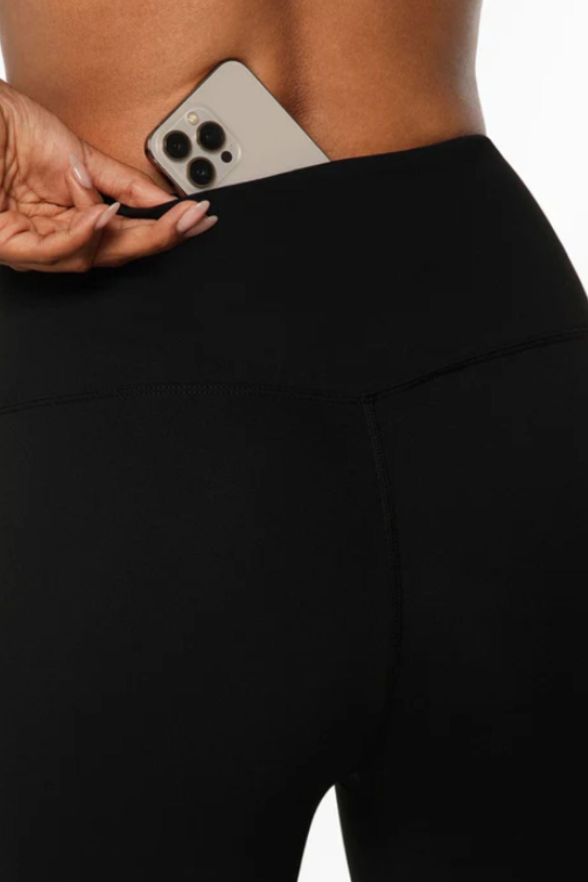 A person places a smartphone in the back waistband pocket of Lorna Jane Lotus No Chafe Phone Pocket 7/8 Leggings, highlighting a close-up of their lower back and hand.
