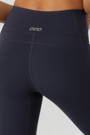 Close-up of a person wearing Lorna Jane Amy No Ride Phone Pocket Ankle Biter Leggings in high-waisted dark navy with visible seams, contouring panel lines, and a small rectangular logo on the back waistband.