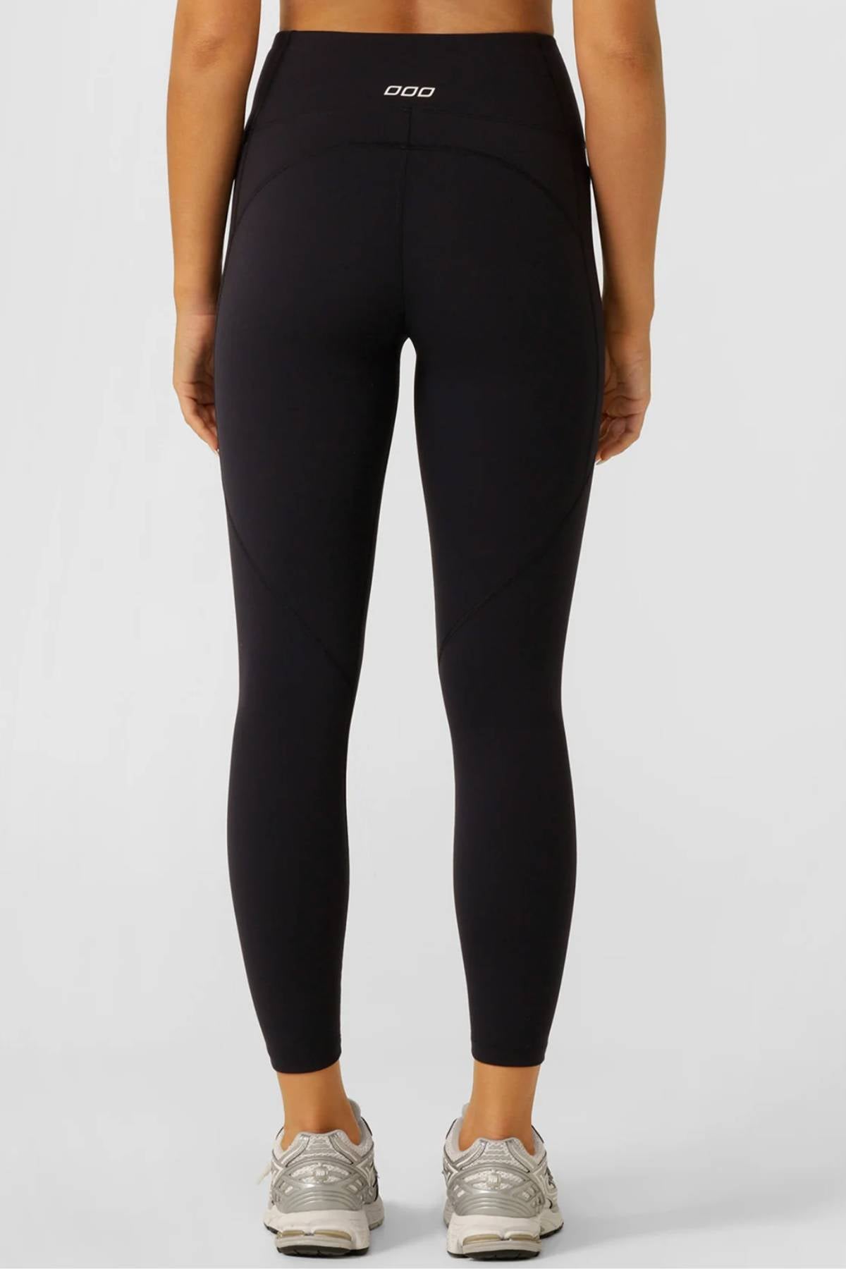 Someone in Lorna Jane Amy No Ride Phone Pocket Ankle Biter Leggings, featuring side phone pockets, and silver athletic shoes stands facing away from the camera against a light background.