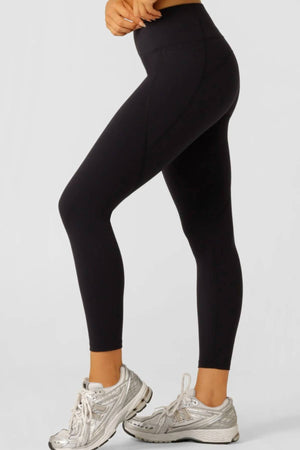 A person wearing black Lorna Jane Amy No Ride Phone Pocket Ankle Biter Leggings, featuring Active Core Stability™ and side phone pockets, stands against a plain light background, shown from mid-torso down in a side view.