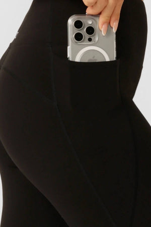 Close-up of a person wearing Lorna Jane Amy No Ride Phone Pocket Ankle Biter Leggings with a smartphone partly in the side pocket. Only part of the lower body and manicured hand are visible.