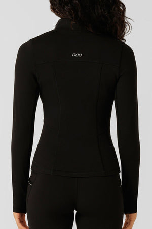 A person with long dark hair is seen from the back wearing a fitted black Lorna Jane Amy Thermal Active Zip Through Jacket, which features a small white logo near the collar, paired with matching pants.
