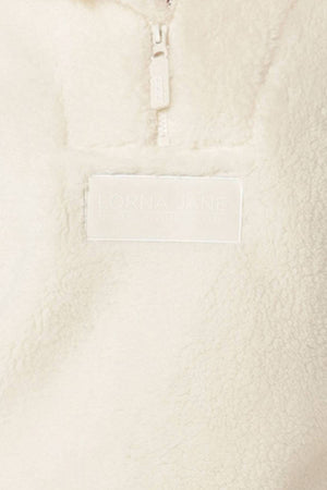 Close-up of the Lorna Jane Everyday Teddy Quarter Zip Sweat, a cream-colored, fuzzy fleece with a zipper and a rectangular "Lorna Jane" patch, made from 100% polyester.