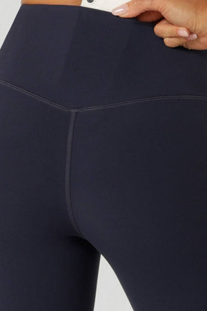 Close-up of a person wearing Lorna Jane Lotus No Chafe Phone Pocket Ankle Biter Leggings in a high rise fit, with their hand on the waistband highlighting visible stitching and stylish premium activewear design.