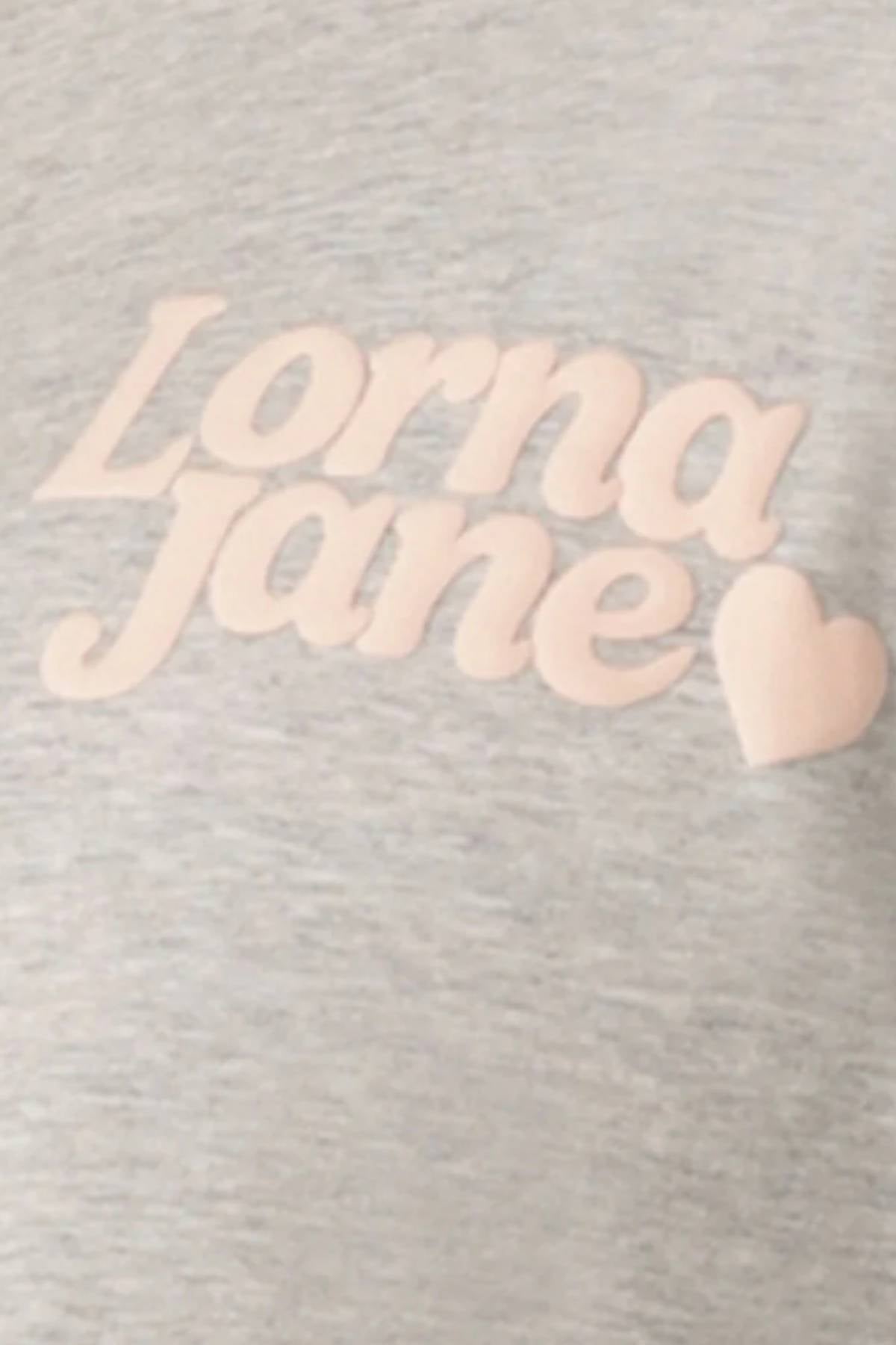 Close-up of the light grey Lorna Jane Heartbeat Relaxed T-Shirt, featuring "Lorna Jane" and a heart in bold light pink cursive. This limited edition tee combines comfort with signature style.