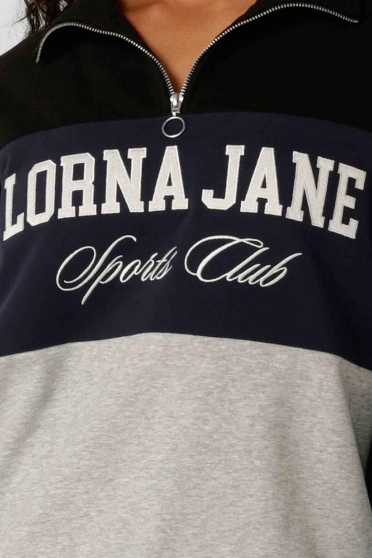 Close-up of the Lorna Jane Heritage Iconic Quarter Zip Sweat, showcasing bold white "LORNA JANE" and cursive "Sports Club" text on a navy and grey color-blocked background.
