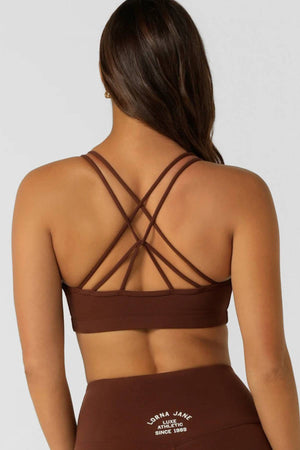 A woman with long brown hair is seen from the back, wearing the Lorna Jane Limited Edition Lotus Crop Sports Bra and matching high-waisted leggings featuring "Lorna Jane Athletic Since 1989" printed on them.