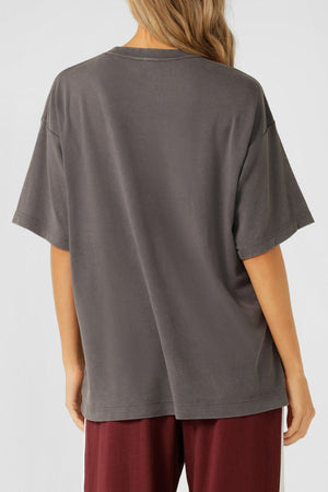 A person with long, wavy blonde hair is seen from behind wearing the Lorna Jane LJ With Love Boyfriend T-Shirt in gray and burgundy pants against a plain light background.