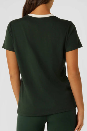 A person with long brown hair is seen from the back, wearing the Lorna Jane Lotus Heritage Ringer T-Shirt in dark green with a white collar and matching pants against a plain, light background.