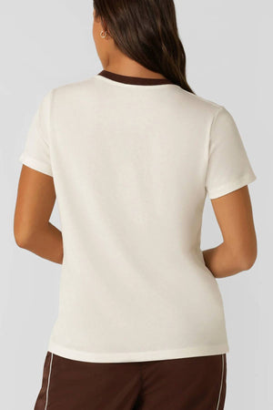 A woman with long brown hair, seen from behind, wears the Lorna Jane Lotus Heritage Ringer T-Shirt—a lightweight, breathable tee with a brown collar—paired with matching shorts against a plain light gray background.