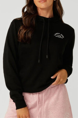 A woman stands with one hand on her hip and the other by her side, wearing the Lorna Jane Lotus Hoodie—a breathable cotton blend hoodie with "Lorna Jane Athletic" on the chest—paired with light pink shorts.