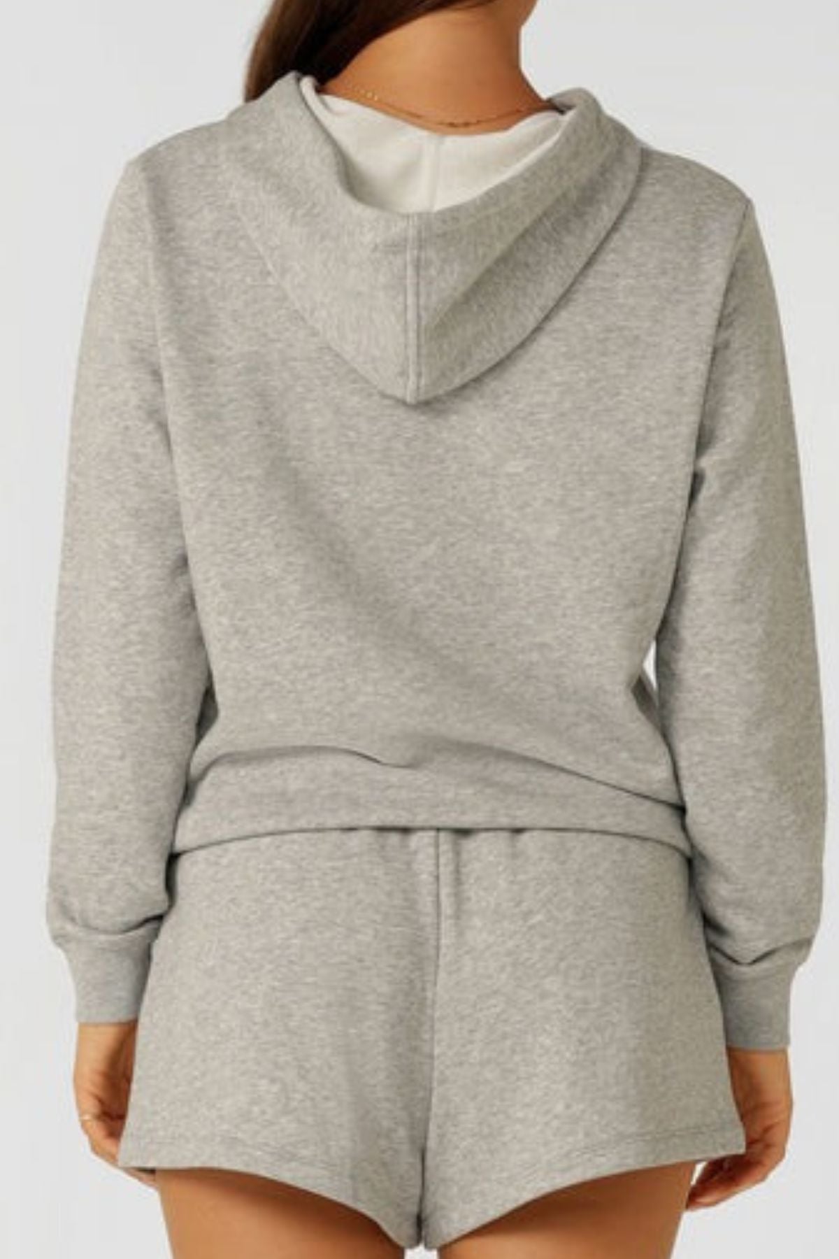 A person is seen from behind wearing the Lorna Jane Lotus Hoodie in light gray cotton blend, paired with matching shorts. The comfortable, breathable outfit stands out against a plain, light background.