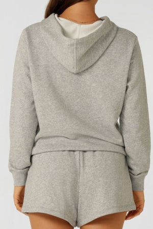 A person is seen from behind wearing the Lorna Jane Lotus Hoodie in light gray cotton blend, paired with matching shorts. The comfortable, breathable outfit stands out against a plain, light background.