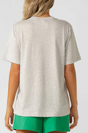 A person with long, blonde hair wears the Lorna Jane Track Star Relaxed T-Shirt in light gray and bright green shorts, shown from the back against a plain light background.
