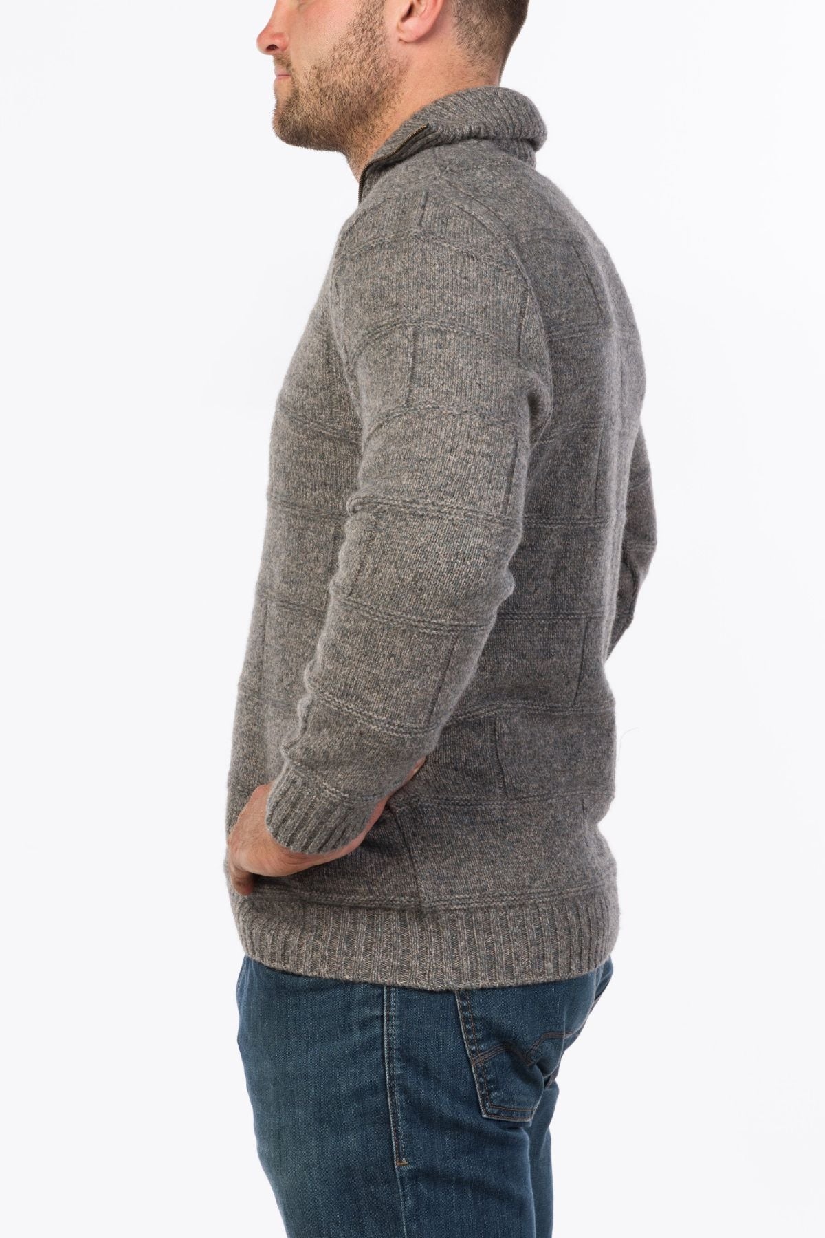 A man in the MKM Marlborough gray Merino Wool Knit sweater and blue jeans stands facing sideways against a plain white background.