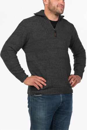 A man stands with hands on hips against a plain white background, wearing the MKM Marlborough dark gray Merino wool knit quarter-zip sweater paired with blue jeans.