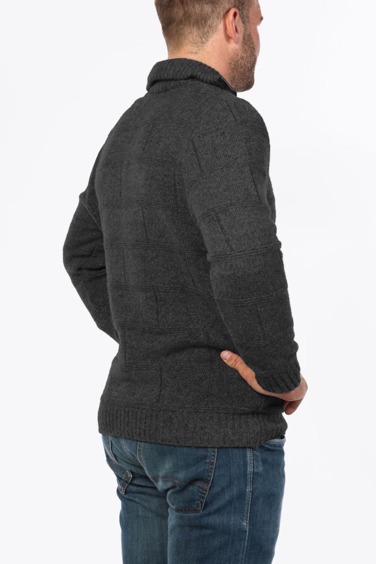 A person stands facing away, wearing the MKM Marlborough dark gray Merino wool knit sweater and blue jeans, with one hand on their hip. The background is plain white.
