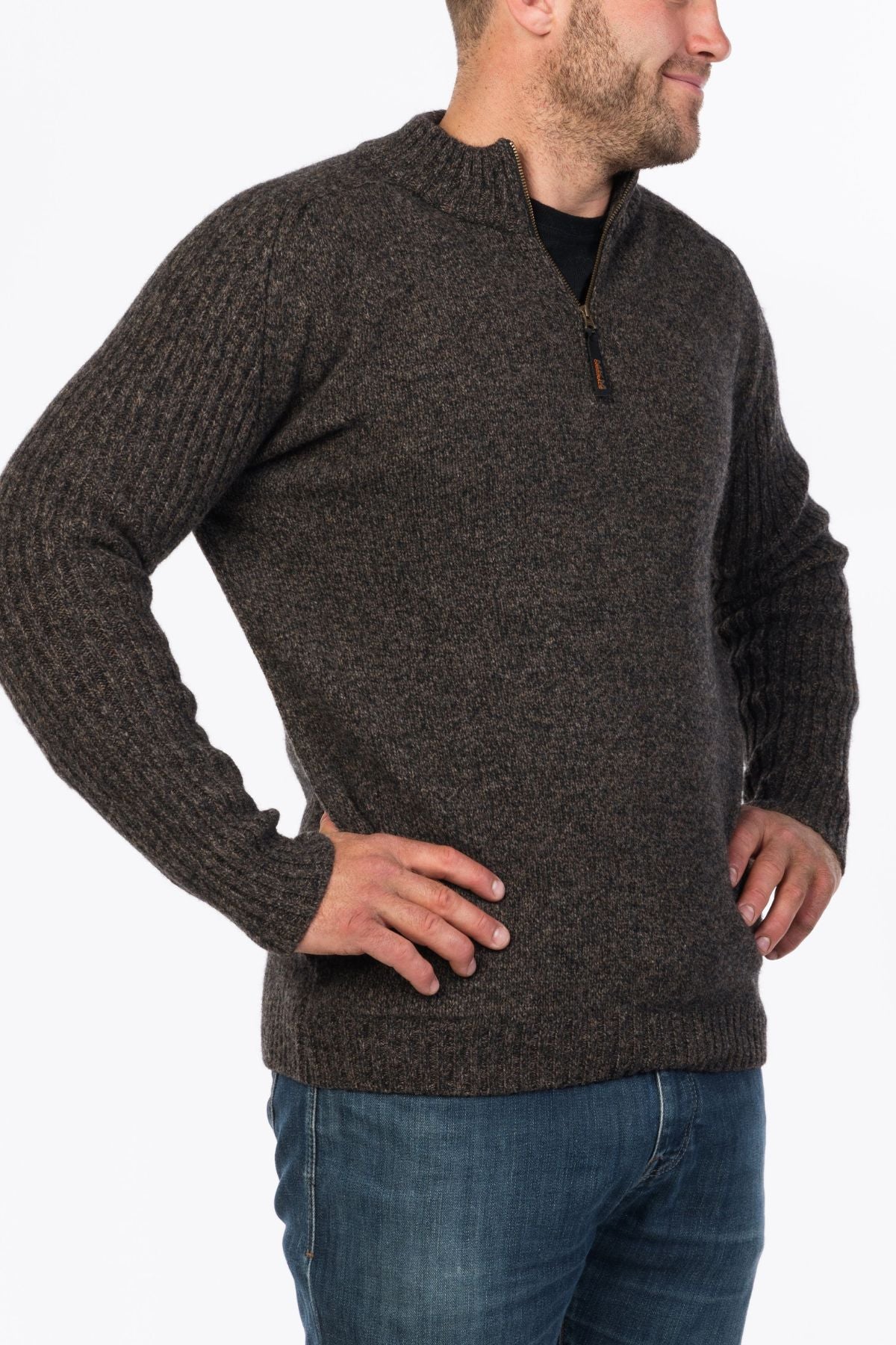 A man wearing the MKM Mount Possum Wool 1/2 Zip Knit in brown and blue jeans stands with his hands on his hips, facing to the right.