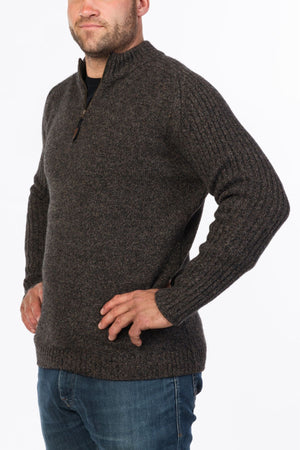 A man wearing the MKM Mount Possum Wool 1/2 Zip Knit in dark gray with long sleeves, paired with blue jeans, stands with his hands on his hips against a white background.