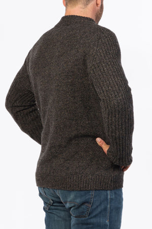 A man wearing the MKM Mount Possum Wool 1/2 Zip Knit in dark brown and blue jeans is standing with his back to the camera, hands on his hips, in front of a plain white background.