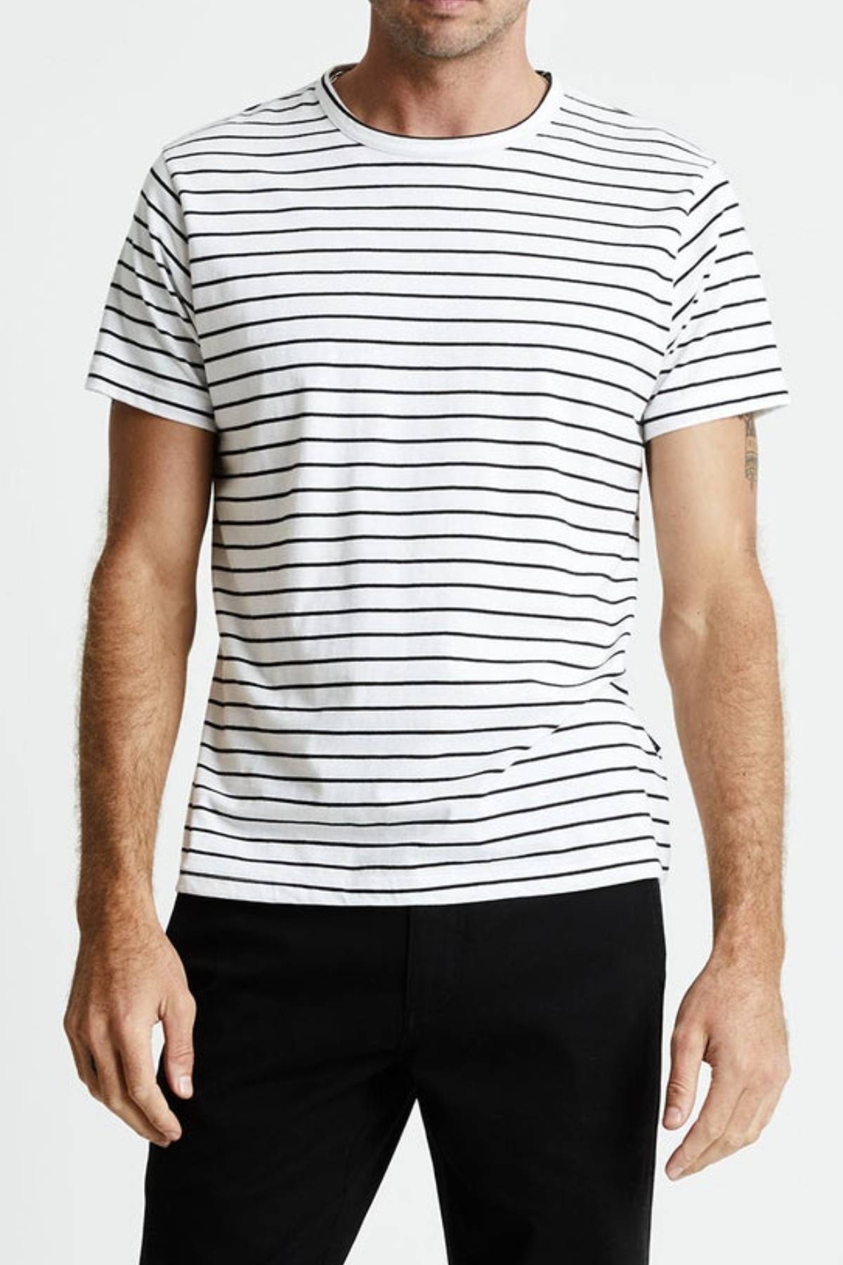 A person is wearing a Mr Simple Breton Stripe Tee, made of 100% organic cotton, with black horizontal stripes and black pants. The T-shirt features short sleeves and a crew neckline. The background is plain white.