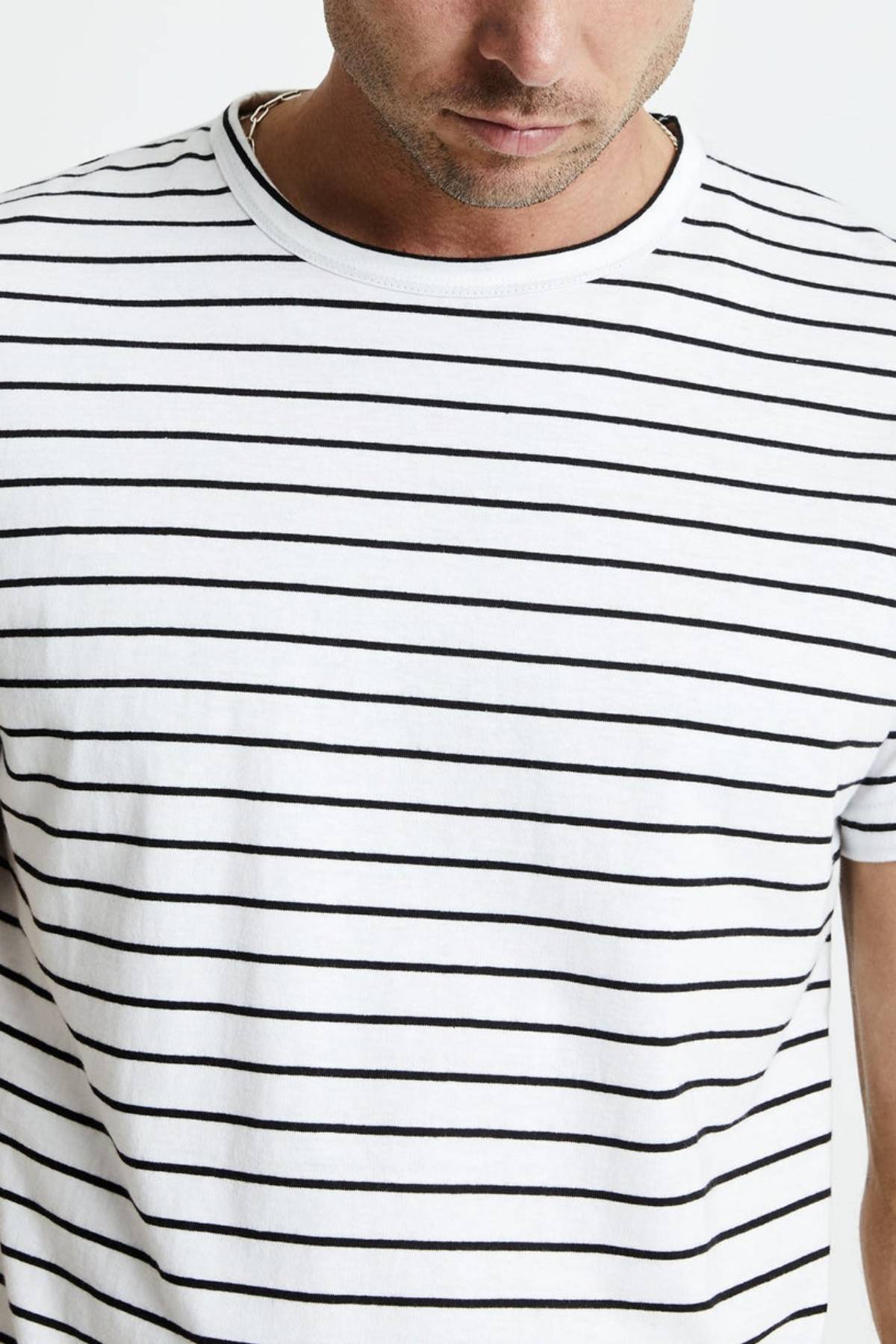 A person is wearing a Mr Simple Breton Stripe Tee made from 100% organic cotton, featuring black horizontal stripes. The image is cropped to show only the lower half of their face and upper torso, highlighting the sustainable fit against a plain, light-colored background.
