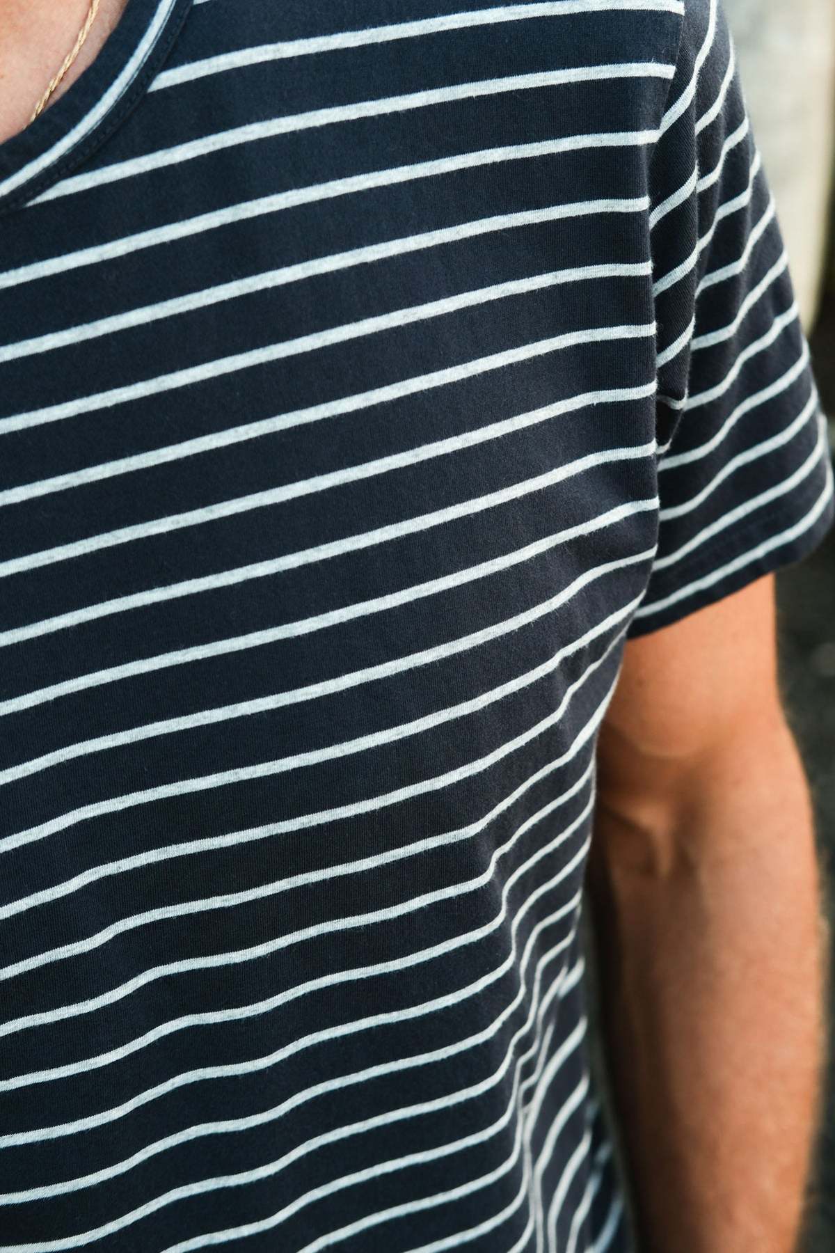 Close-up of someone wearing the Mr Simple Breton Stripe Tee, a sustainable top made from organic cotton. The image captures the upper part of the shirt and part of the arm, highlighting its timeless design.