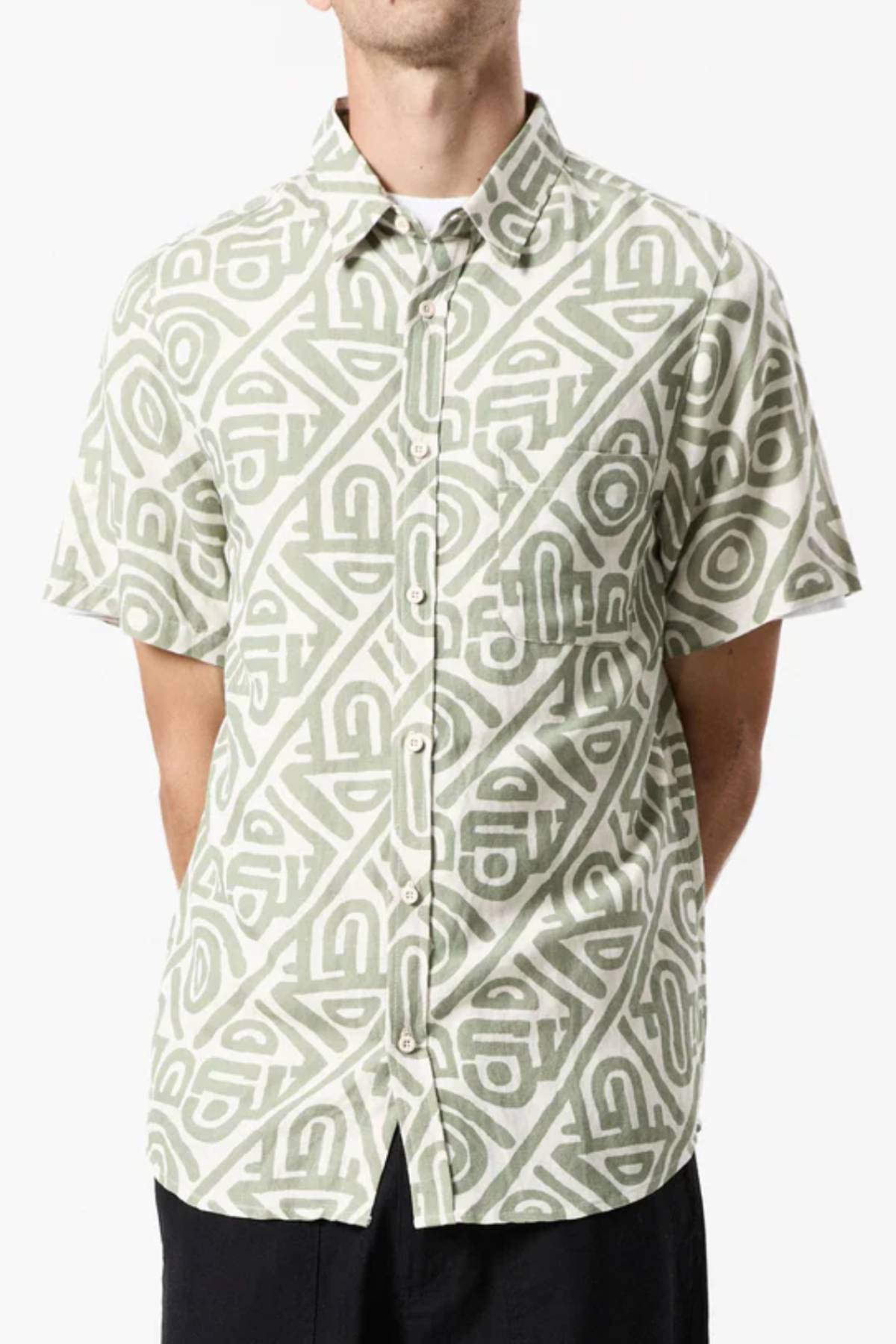 A person wearing the Mr Simple Earl Short Sleeve Shirt with a loose fit and geometric green and white pattern pairs it with black pants, standing forward with hands behind their back.