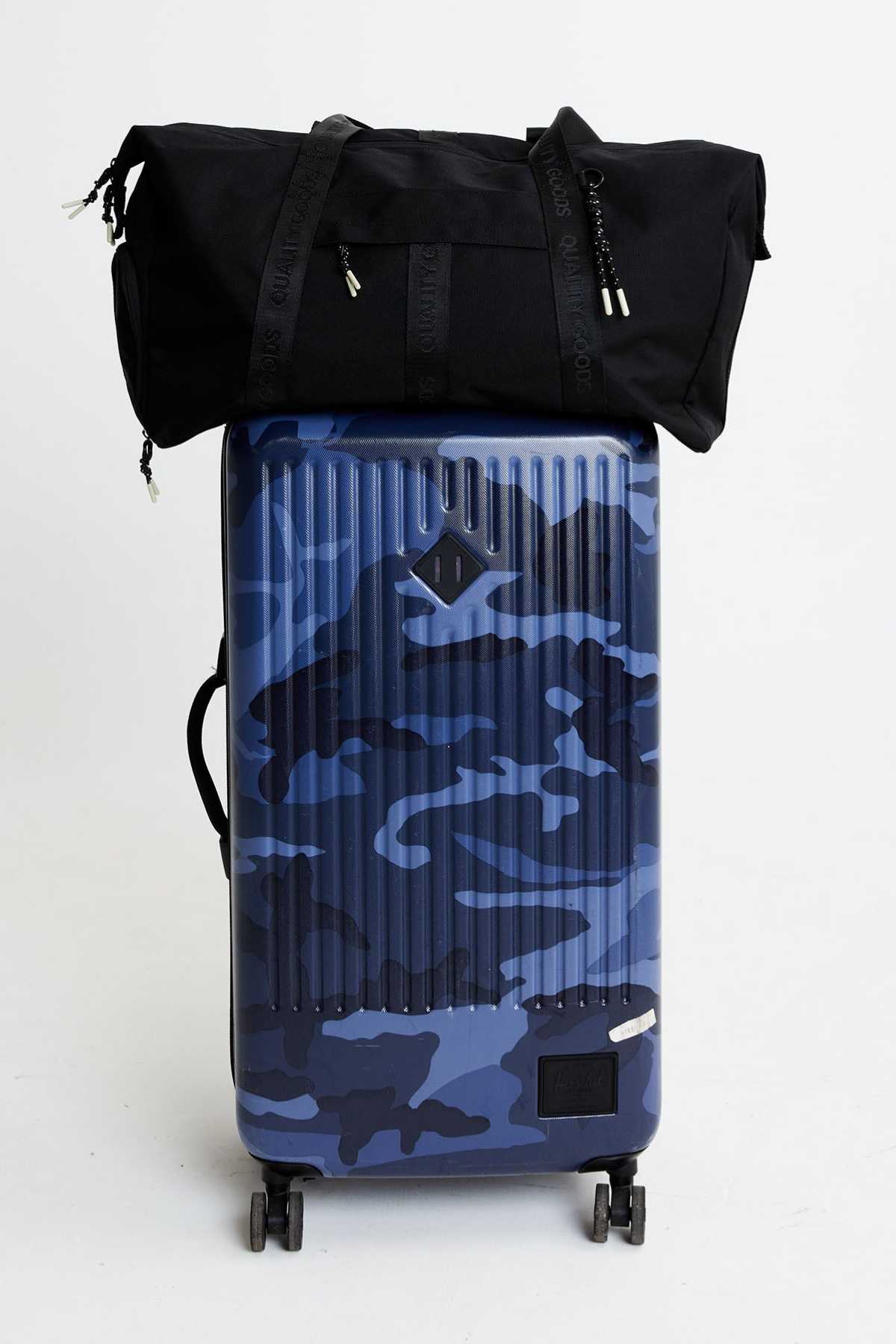A blue camouflage hard-shell suitcase with four wheels and a black Mr Simple Nelson Duffle bag featuring a trolley sleeve, both displayed against a plain white background.