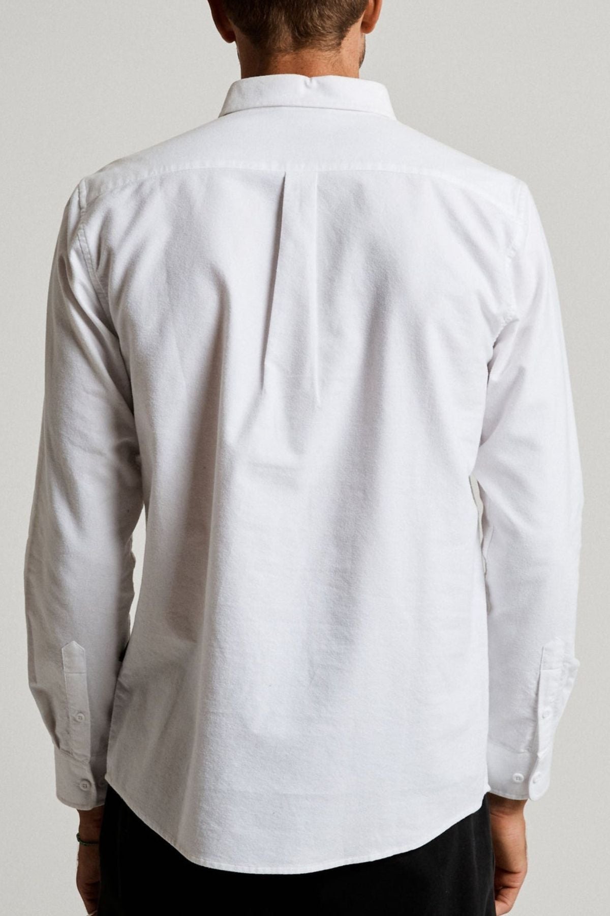 Someone is seen from behind wearing the Mr Simple Oxford Shirt, a slim-fit, long-sleeved white collared shirt, standing against a plain light background.