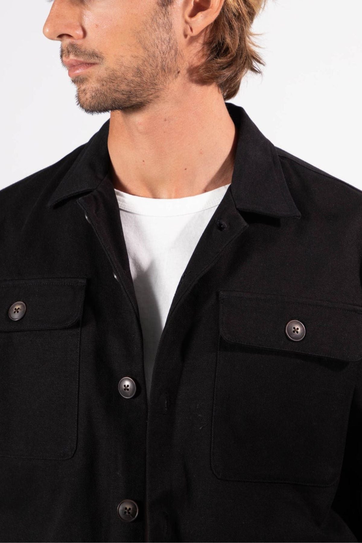 A man with light brown hair and facial hair wears the Mr Simple Stockyard Sherpa Jacket in black over a white t-shirt. The cropped photo highlights his head turned sideways and upper torso, showcasing classic Mr Simple style against a plain background.